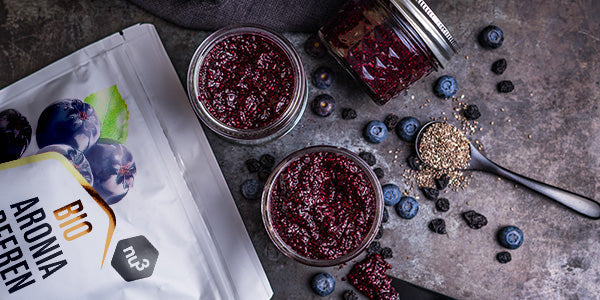 nu3 Aroniabeeren liegen neben Marmelade und frischen Beeren 