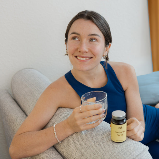 Frau mit Glas Wasser und Curcuma Kapseln auf Sofa